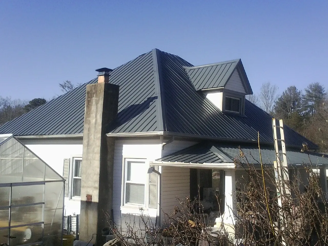 Dark blue standing seam metal roof on a white farmhouse with dormer — Slate & Tile Roof Repair by Roofing Brothers in Warm Springs